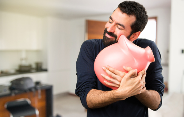 Мужчина обнимает розовую свинью копилку 