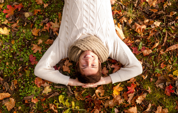 Улыбающийся мужчина в свитере лежит на опавших листьях 