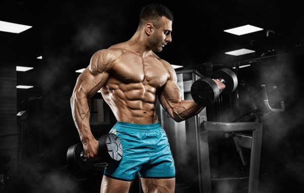 Strong pumped man in shorts with dumbbells in his hands