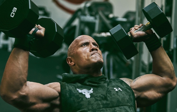 Американский актер, сильный мужчина Дуэйн Джонсон с гантелями в спортзале