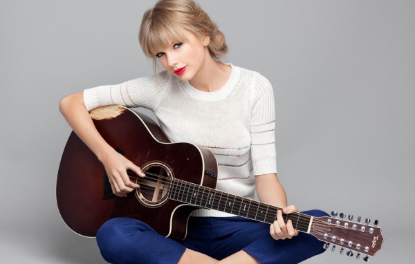 Красивая певица Тейлор Свифт с гитарой на сером фоне