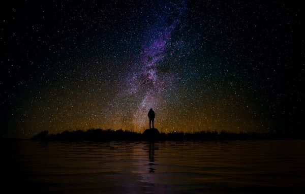 Силуэт человека стоит на камне у воды под звездным небом