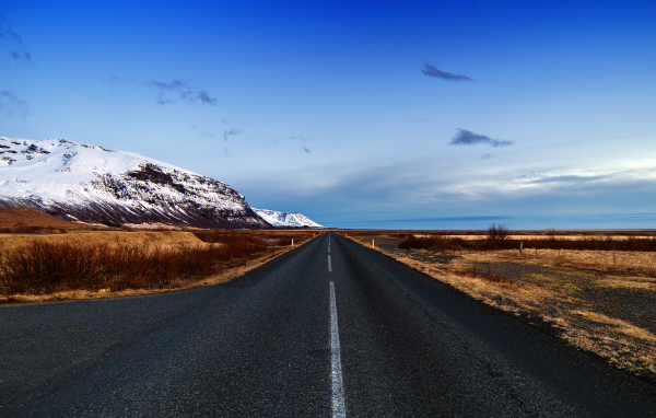 Ровная асфальтовая дорога у заснеженных гор