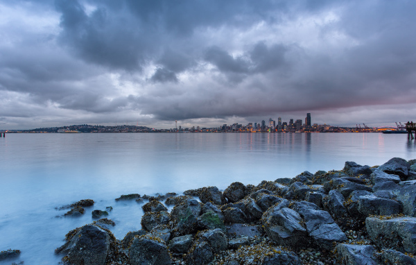 Камни на берегу реки на фоне города под пасмурным небом