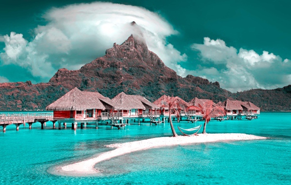 Дома на сваях в голубом океане на фоне горы под белыми облаками