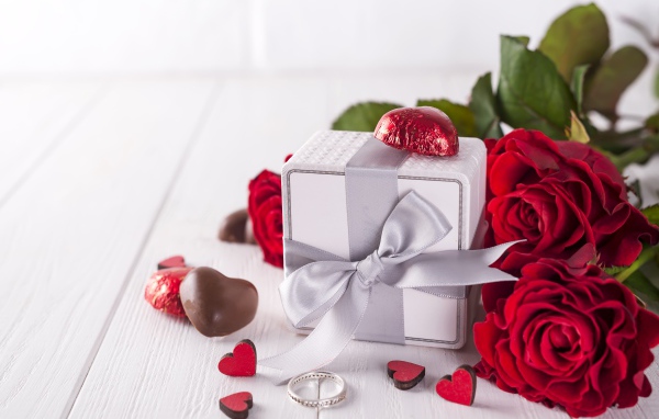 A gift on the table with sweets and a bouquet of red roses
