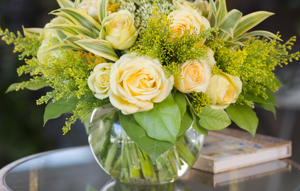 Красивый букет роз с зелеными листьями в в вазе на стеклянном столе