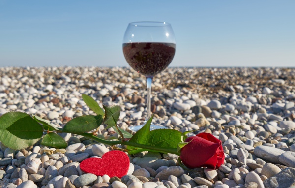 Красная роза на морской гальке с сердечком и бокалом вина
