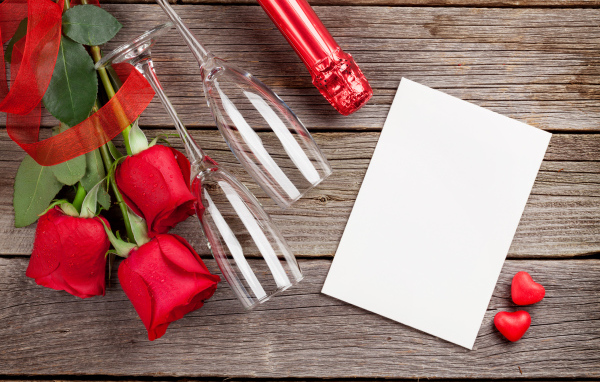 Белый лист бумаги на деревянном столе с бокалами и красными розами