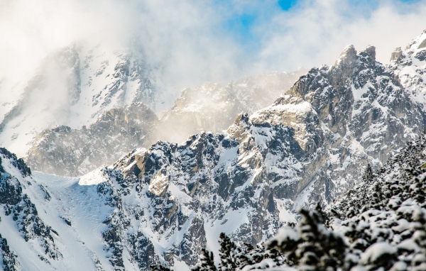 Заснеженные вершины гор под белыми облаками в голубом небе