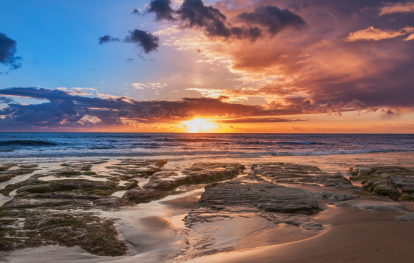 Мокрый песок и камни на берегу океана на закате солнца