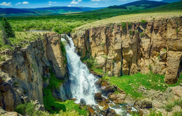 Быстрая вода водопада стекает по утесу на фоне голубого неба
