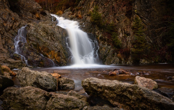 Быстрая вода водопада стекает по камням в горную реку