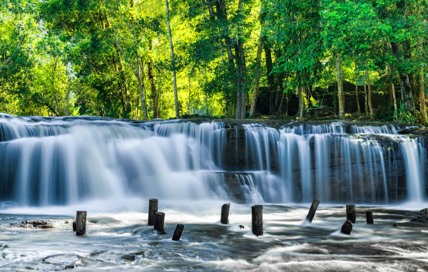 Водопад стекает с камней у зеленых деревьев