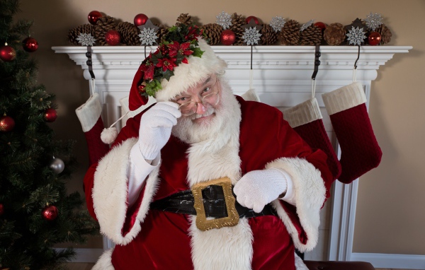 Санта Клаус в очках сидит у камина у новогодней елки