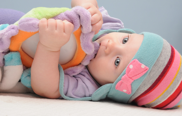 Младенец в шапке грызет мягкую игрушку