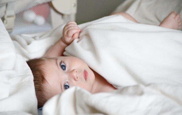 Маленький грудной голубоглазый ребенок лежит под белым покрывалом 