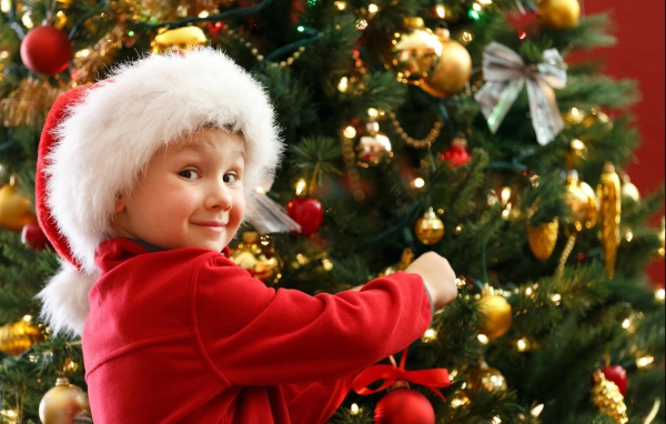 Мальчик в шапке Санта Клауса наряжает елку