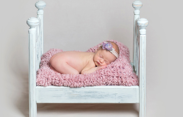 Милый грудной ребенок спит в маленькой кроватке на сером фоне