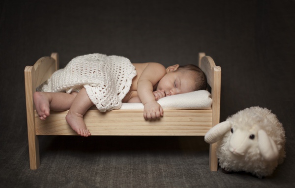 Маленький ребенок спит на деревянной кроватке с игрушкой