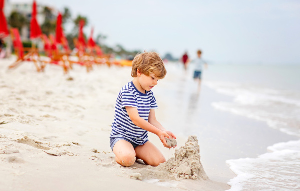 Маленький мальчик строит замок из песка на пляже