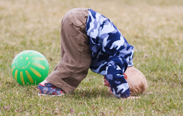 Маленький мальчик играет на траве с мячом