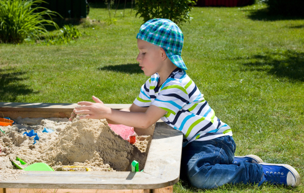 Маленький мальчик играет в песке на зеленой траве