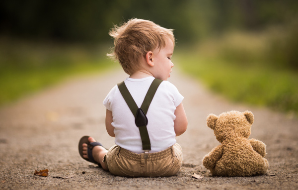 Маленький мальчик сидит на дороге с игрушечным мишкой