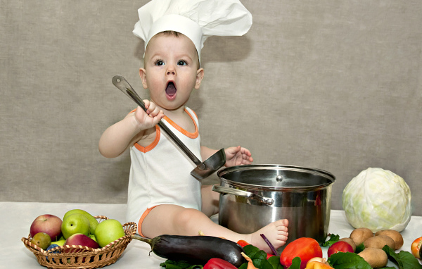 Маленький поваренок с кастрюлей на столе с овощами