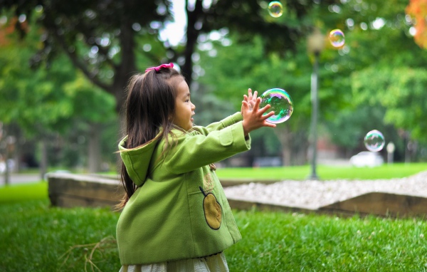 Маленькая девочка ловит мыльные пузыри на зеленой траве