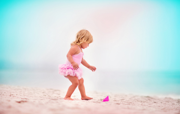 Маленькая девочка в розовом купальнике на песке