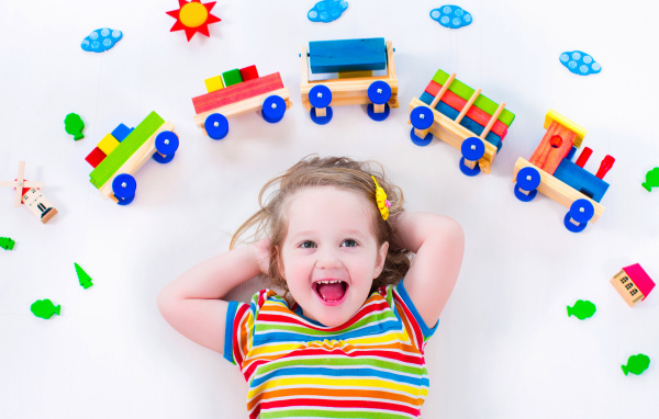 Маленькая девочка на сером фоне с игрушечным паровозом 