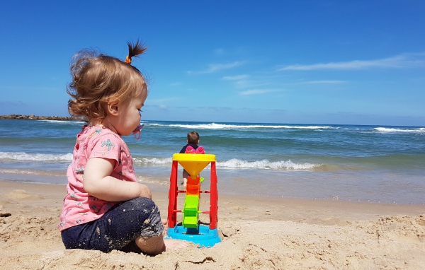 Маленькая девочка играет на песке у моря