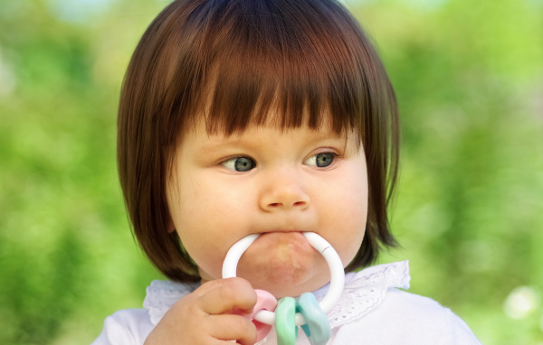 Маленькая девочка с погремушкой во рту