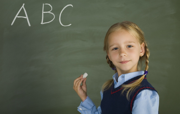 Маленькая школьница пишет буквы на доске 
