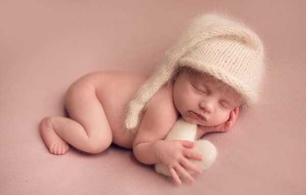 Маленький спящий ребенок в теплой шапке на розовом фоне