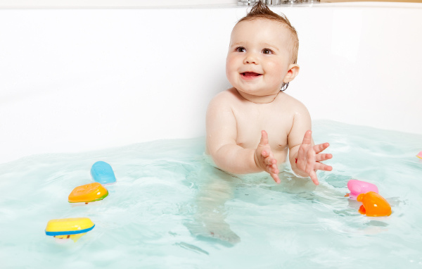 Маленький улыбающийся ребенок с игрушками в ванной 