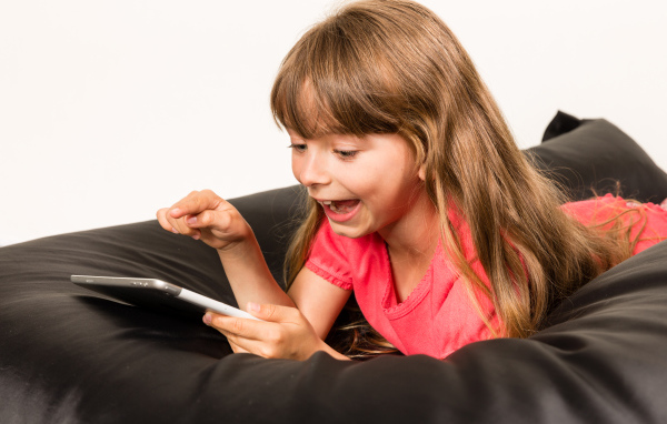 Маленькая улыбающаяся девочка лежит с планшетом