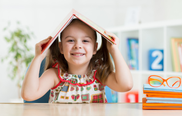 Маленькая улыбающаяся девочка с книгой на голове