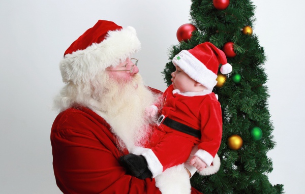 Дед Мороз держит на руках маленького ребенка у елки