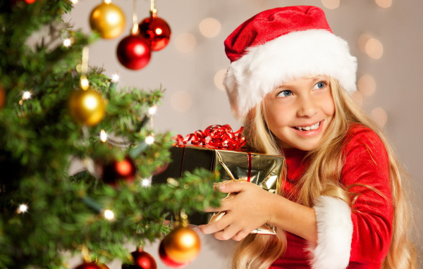 Улыбающаяся девочка блондинка с подарком у елки на новый год 