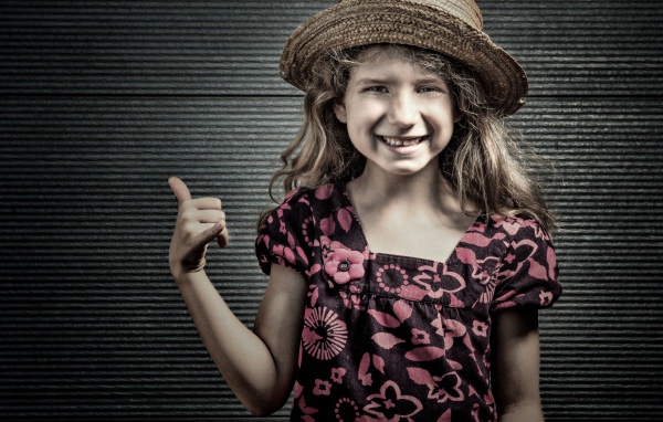 Улыбающаяся девочка в соломенной шляпе у стены 