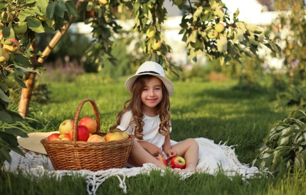 Улыбающаяся девочка сидит на зеленой траве с яблоками