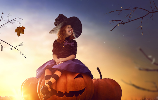 Улыбающаяся девочка сидит на тыкве в костюме на Хэллоуин 