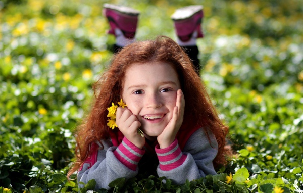 Улыбающаяся рыжеволосая девочка лежит на зеленой траве