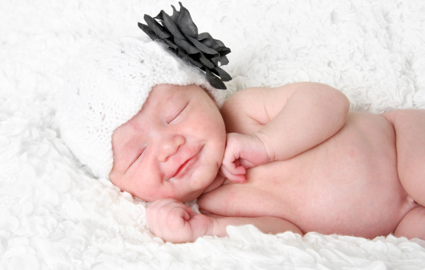 Улыбающийся спящий ребенок в белой вязаной шапке с цветком