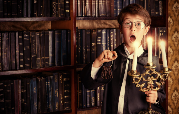 Удивленный мальчик с подсвечником со свечами в библиотеке