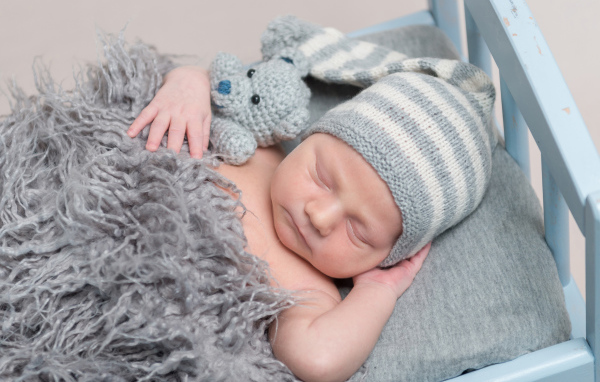 Младенец в вязаной шапке спит с игрушкой под меховым одеялом