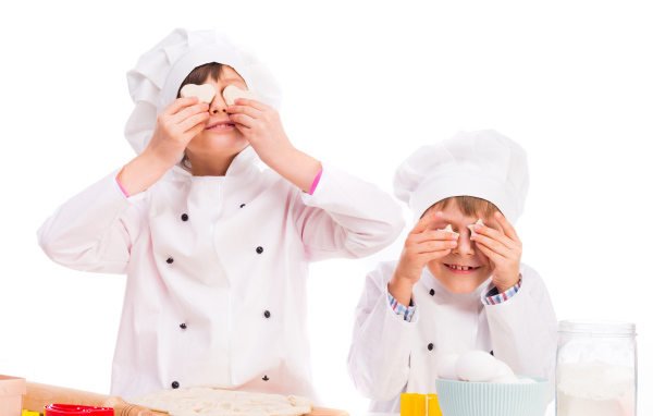 Два маленьких мальчика в костюмах повара на кухне делают печенье