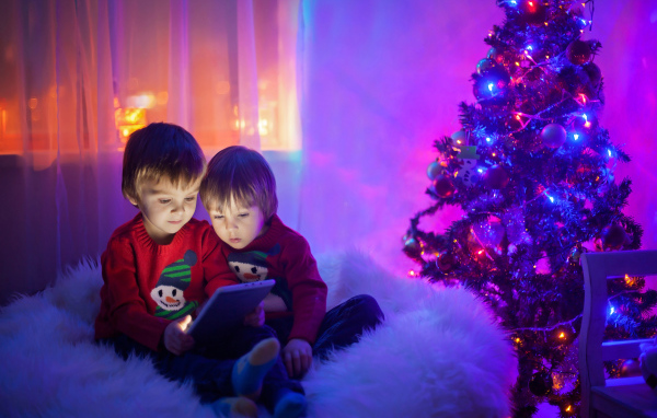 Два маленьких мальчика смотрят мультики у новогодней елки